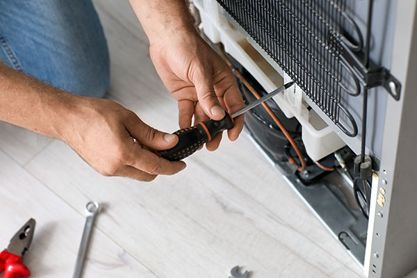 Worker repairing fridge in kitchen, closeup